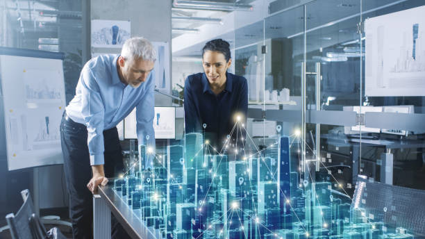 istock Male and Female Architects Work with Holographic Augmented Reality 3D City Model. Technologically Advanced Office Professional People Use Virtual Reality Modeling Software Application. 921019730