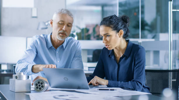 istock Experienced Male and Female Industrial Engineers Discuss ongoing Project while Working on a Laptop. They Design Machinery Component. 921020080