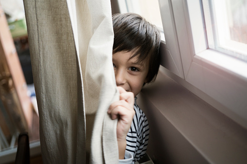 Sixth year old boy hiding behind the curtain