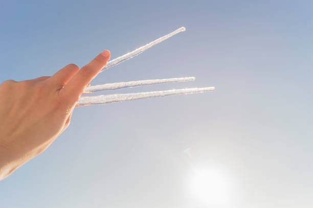 Three long icicles in a female hand against a blue sky background
