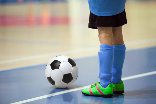 allenamento di calcio a 5 per bambini. giovane giocatore di calcio indoor con un pallone da calcio in un palazzetto dello sport. giocatore in uniforme blu. background sportivo. - futsal indoors soccer ball soccer foto e immagini stock