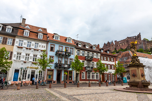 Heidelberg: People walking on Kornmarkt square in Heidelberg old town, Germany. Madonna statue on foreground and Heidelberg castle on the background