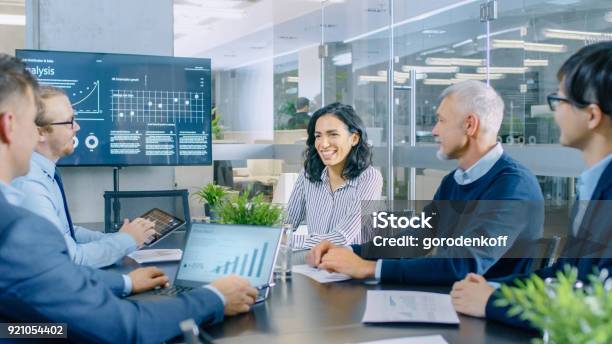 Diverse Team Of Executives Have Meeting In A Conference Room They Share Opinions Statistics Show On Laptops And Tablets In The Background Tv Screen With Relevant Information About Companys Growth Stock Photo - Download Image Now