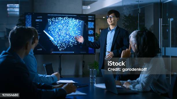 In The Conference Room Chief Engineer Presents To A Board Of Scientists New Revolutionary Approach For Developing Artificial Intelligence And Neural Networks Wall Tv Shows Their Achievements Stock Photo - Download Image Now