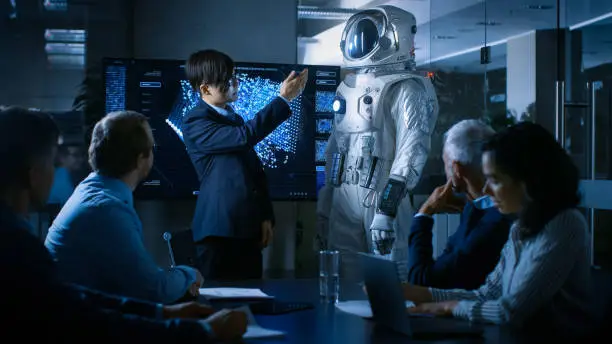 Photo of In the Conference Room of the Center of Technology Chief Engineer Presents Next Generation Space Suit to a Board of Directors. Completely Original Design with Integrated AI and Neural Network Systems.