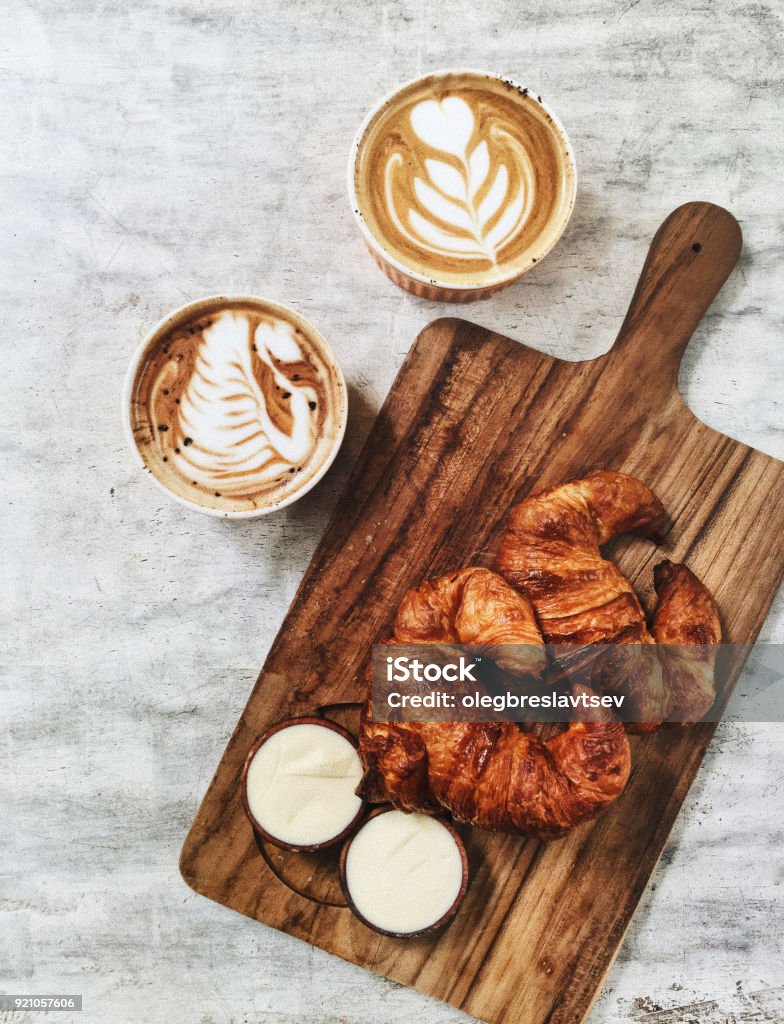 Two fresh crispy butter croissant on wooden plate and two hot aroma cappuccino. French breakfast, textured background Croissant Stock Photo