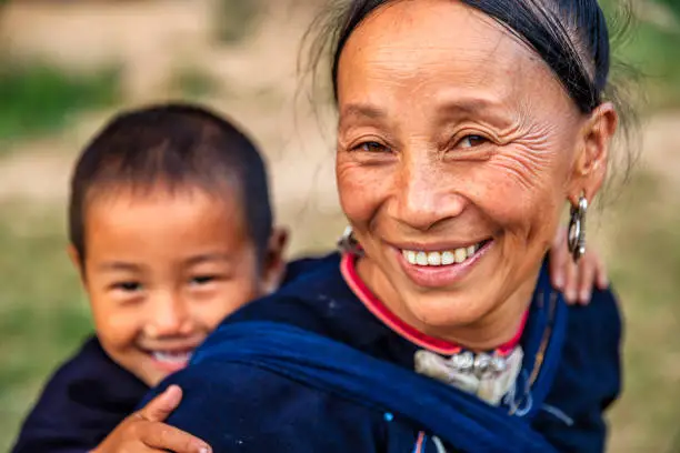 Laotian mom with her little boy, wearing traditional Lantan tribe clothes, walking together in a Lantan village in Northern Laos