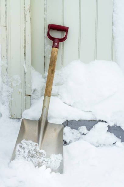 Shovel in the snow outside by an old wood wall