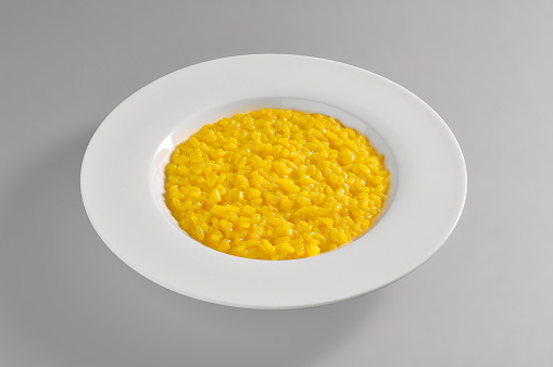 Round dish with yellow Milanese risotto  isolated on grey background