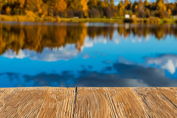 istock Empty rustic wood table top on  blurred colorful autumn landscape background with fall forest and blue sky with cloudscape reflection on the lake. Can montage or display your products 921104280