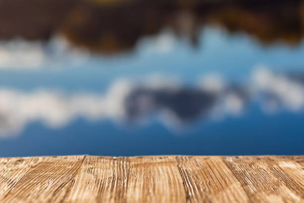 istock Empty rustic wood table top on  blurred colorful autumn landscape background with fall forest and blue sky with cloudscape reflection on the lake. Can montage or display your products 921104360