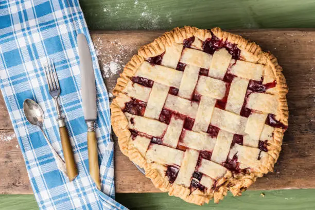 A pie on a wooden surface on a green table next to a rolling pin and some spilled flour