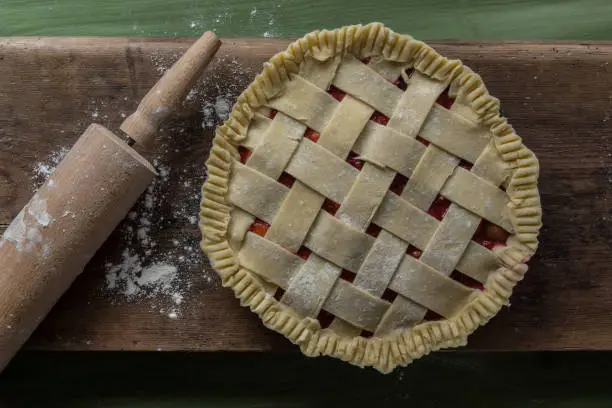 A unbaked pie on a wooden surface on a green table next to a rolling pin and some spilled flour