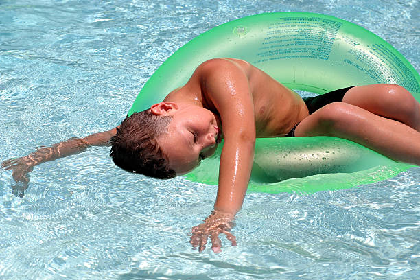 Funny photo of baby boy swimming with fun on inflatable swim ring in clear aqua park pool. Top view. Healthy family lifestyle, children with parents outdoor water sports activity on summer holidays.