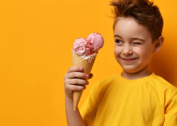 Baby boy kid eating strawberry ice cream in waffles cone and winking on yellow stock photo