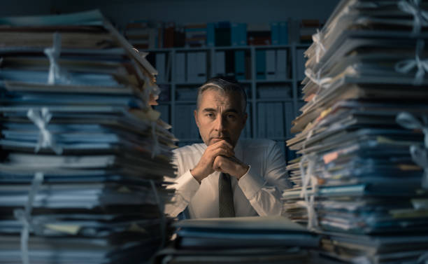 Business executive overloaded with work Stressed exhausted business executive working in the office late at night with piles of paperwork, he is overloaded with work: management and deadlines concept bureaucracy stock pictures, royalty-free photos & images