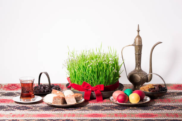 Novruz concept wtih tea in tulip shape glass and wheat grass decorated with red ribbon Novruz setting table decoration, tea in  tulip shape glass on ethnic motives rustic table cloth with wheat grass, dyed eggs, traditional sweets, samovar, new year sring celebration, nature awakening baku photos stock pictures, royalty-free photos & images