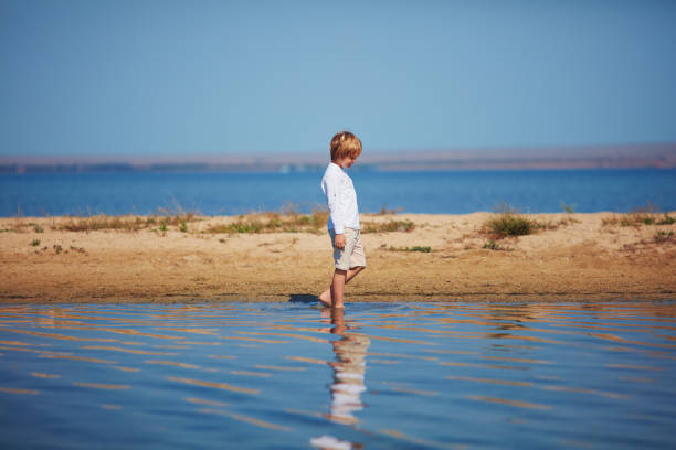 cute young boy walking in reflected water on lakeshore