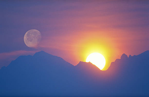 sun and moon behind mountain stock photo
