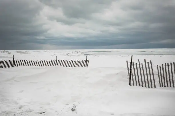 Large snow buildup on beach with wooden fence and cloudy sky