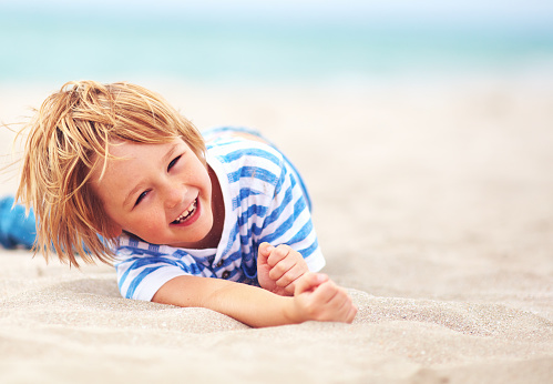 cute happy laughing boy, kid having fun on sandy beach, summer vacation