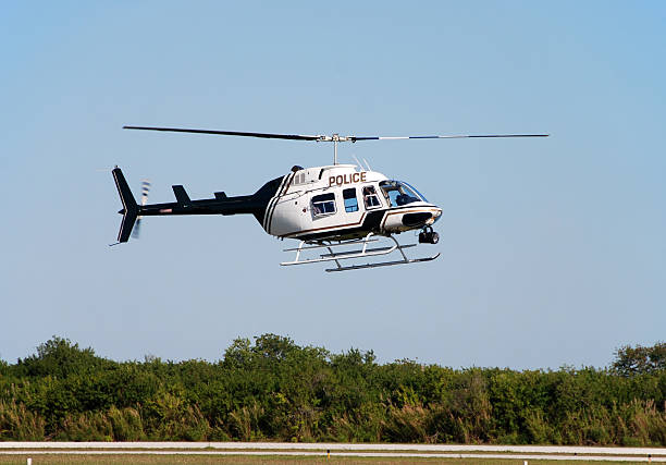 police helicopter flying above a tree line on a sunny day - helikopter stockfoto's en -beelden