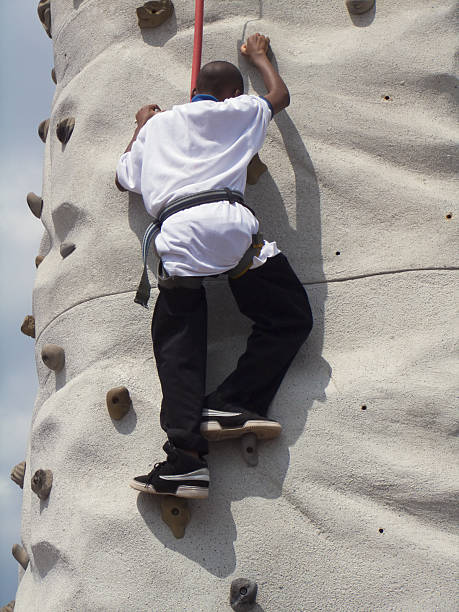 An African-American teen boy tests his strength and challenges himself on a rock climbing wall.