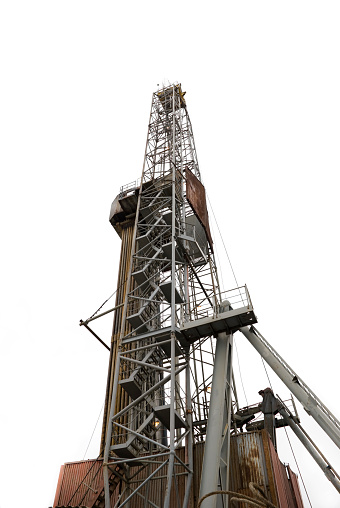 A metal crane near a huge oil energy tank under a blue cloudy sky