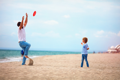 father and son enjoying summer vacation, playing beach activity games near the sea, family throwing flying disk