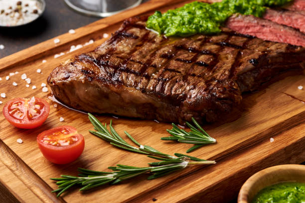 gegrillte black angus-steak mit tomaten, knoblauch mit chimichurri-sauce auf fleisch schneidebrett. - chimichurri horizontal beef steak stock-fotos und bilder