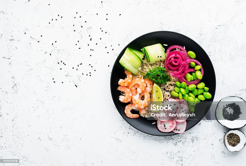 Receta de pescados y mariscos frescos. Camarón meter plato con Gambas frescas, arroz, pepino, cebolla dulce en vinagre, rábano, soja habas edamame repartido con sésamo blanco y negro. Bolo de poke concepto alimenticio. Vista superior - Foto de stock de Poke - Alimento libre de derechos