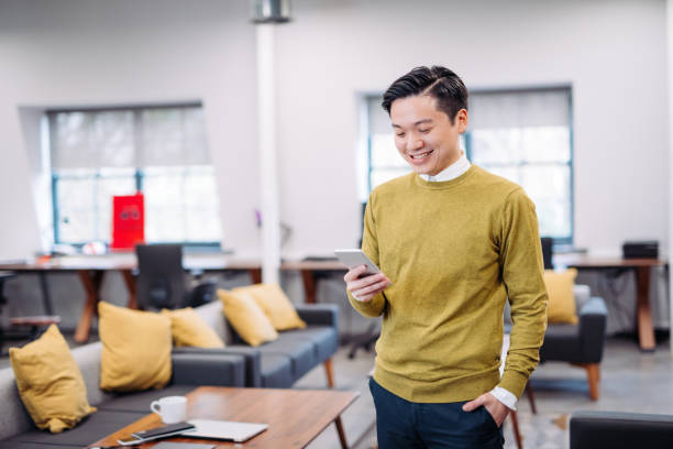 Taiwanese man using smart phone to send text message Young start-up founders sitting in coworking space with colleagues and developing new project ideas that will cover many Asian countries and connect the market players around Taiwan, China, South Korea and Japan. International cooperation in East Asia is a key to success. taiwan people stock pictures, royalty-free photos & images