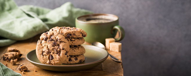 Chocolate chip cookies on green plate with cup of coffee on old wooden table. Selective focus. Copy space. Banner.