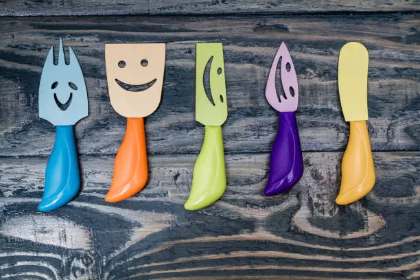 Knifes and forks with smiley faces on blue wooden background