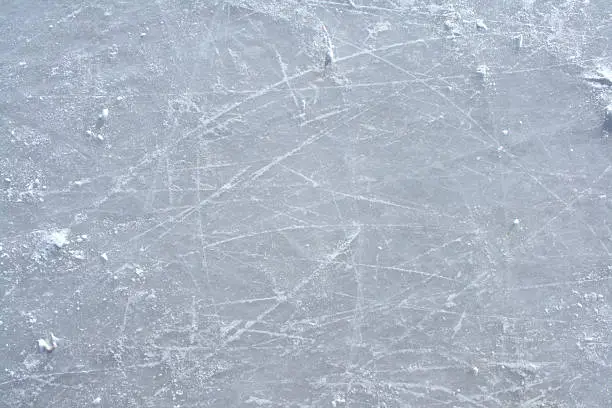 Surface of an outdoor ice rink replete with skate marks.