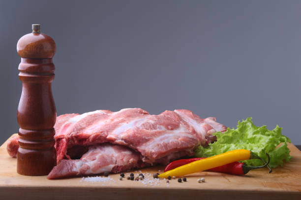 istock Raw Ribs on a rustic cutting board with salt, pepper and grinder for spices . Black Background for copy space. Top View. 921302058