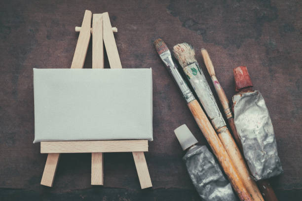 istock Artist paintbrushes, paint tubes and small easel with canvas closeup. Top view. 921308656