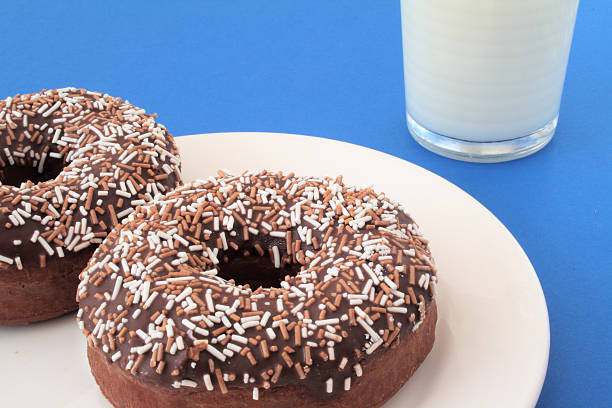 Due ciambelle al cioccolato e un bicchiere di latte - foto stock