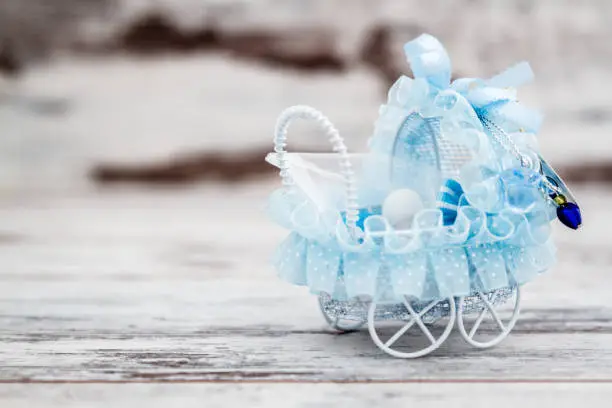 Blue toy baby carriage prepared as a gift for baby shower on white wooden background