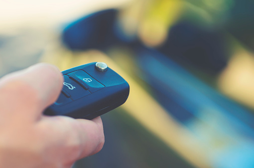 Unlocking car with car key. Tight crop with part of womanâs hand. The car is out of focus in the background