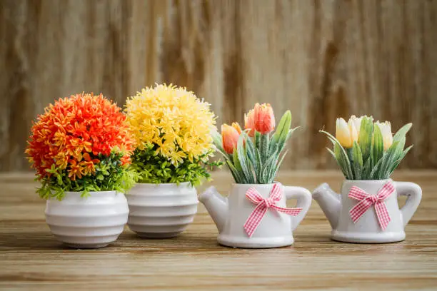 Artificial colorful flowers in white pots on wooden background