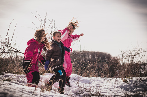 Three cute small child jumping on the hill at winter, wearing warm clothes