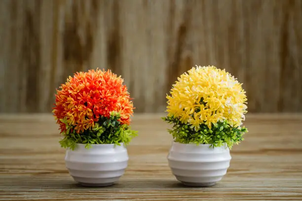 Artificial colorful flowers in white pots on wooden background