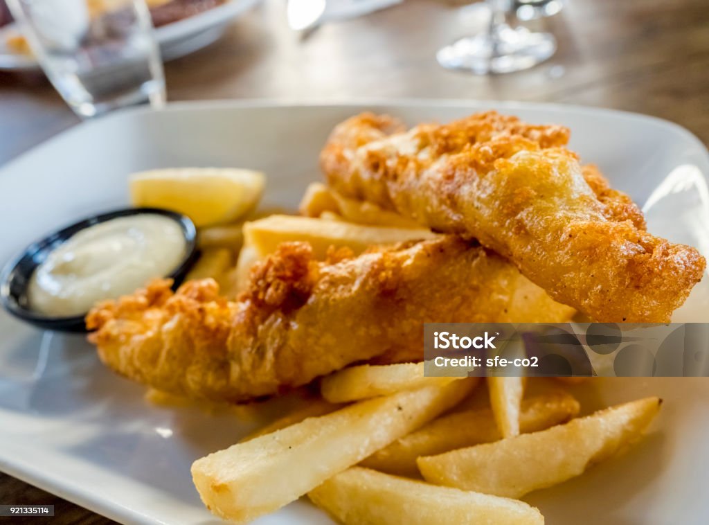 Battered fish and chips Battered fish and chips (fries) freshly cooked to golden brown, served on a plate with a wedge of lemon and some sauce. Fish and Chips Stock Photo