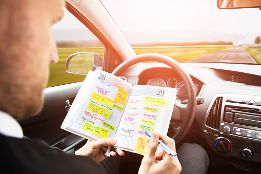 Close-up Of A Businessman Writing Schedule In Diary With Pen Inside Self Drive Car