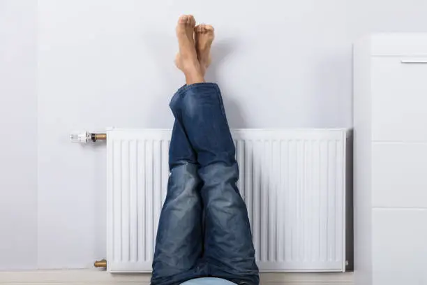 Man Warming Up His Feet On White Radiator At Home