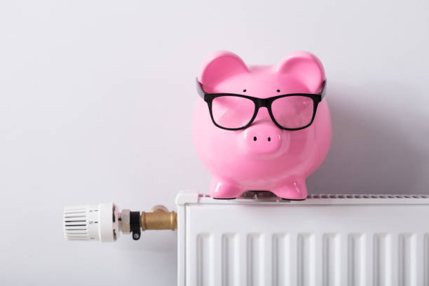 Thermostat And Piggy Bank With Eyeglasses On Radiator Close-up Of Thermostat And Piggy Bank With Eyeglasses On Radiator Against White Wall thermostat photos stock pictures, royalty-free photos & images