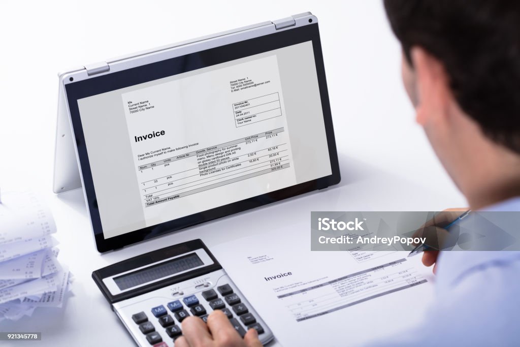 Businessman Calculating The Invoice Close-up Of Businessman Calculating The Invoice Using Hybrid Laptop And Calculator At Workplace Accountancy Stock Photo