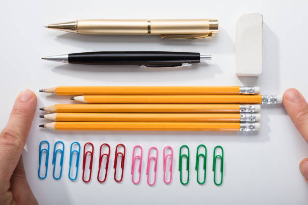 Person's Finger Arranging The Pencils With Row Of Pins Rubber And Pen On White Background