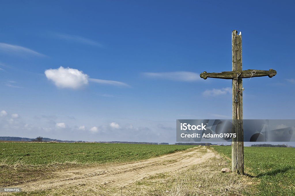 Old cross standing on the side of a road Old wooden cross at country road. Green grass and blue sky. Agricultural Field Stock Photo